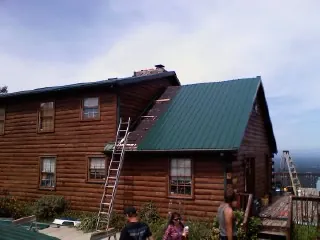 Green metal roof going on a two story log home with ladders set in Lewiston