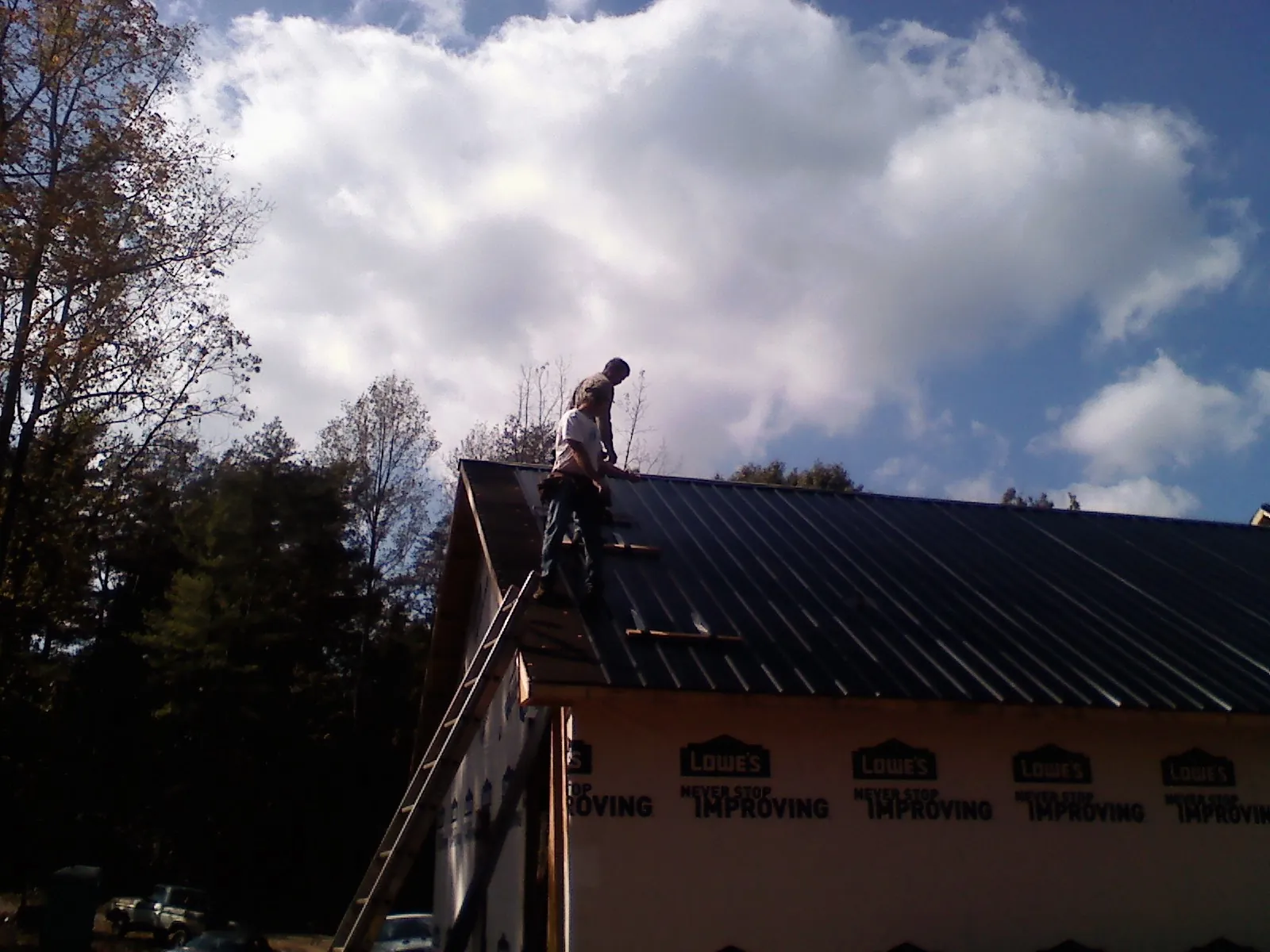 Roofer fastening dark metal panels high against a cloudy sky, from a Roof Inspection job in Lewiston